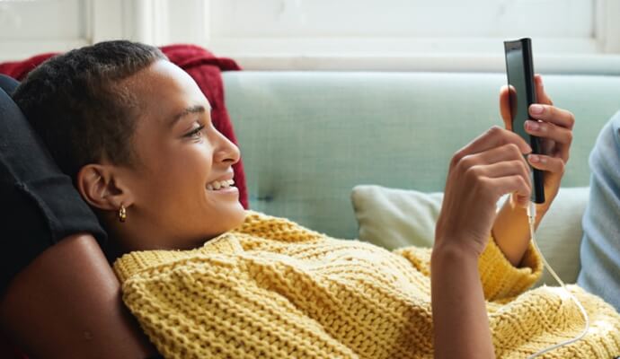 woman on couch looking at cell phone launching Norton 360 with AntiVirus Plus.